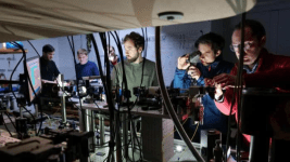 Bir laboratuvarda karmaşık optik deney düzeneği üzerinde çalışan bilim insanları.